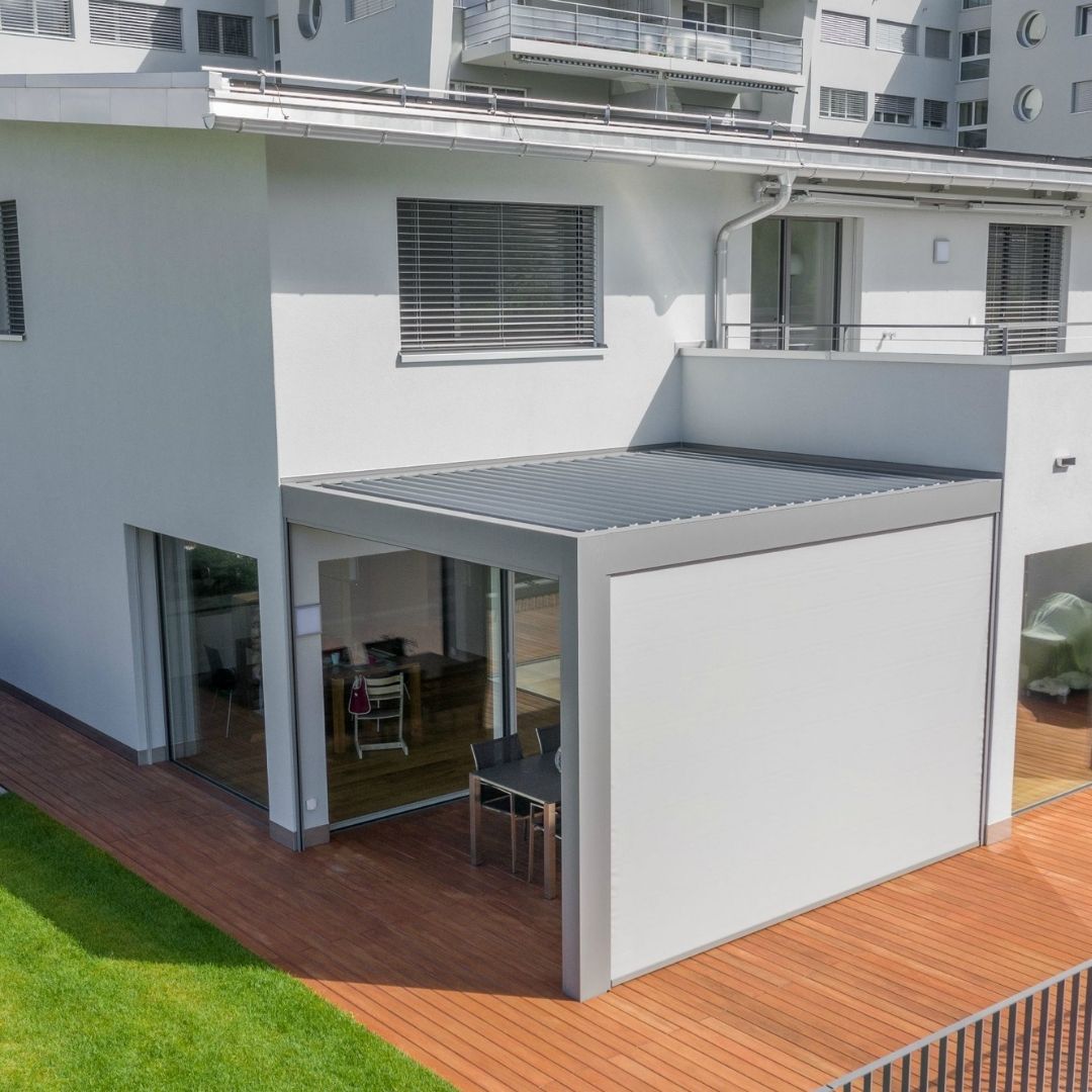 Modernes SKL 140 Lamellendach von Thermogreen an einem Wohnhaus, mit geschlossenem seitlichem Screen und Glas-Schiebetüren als Wetterschutz.