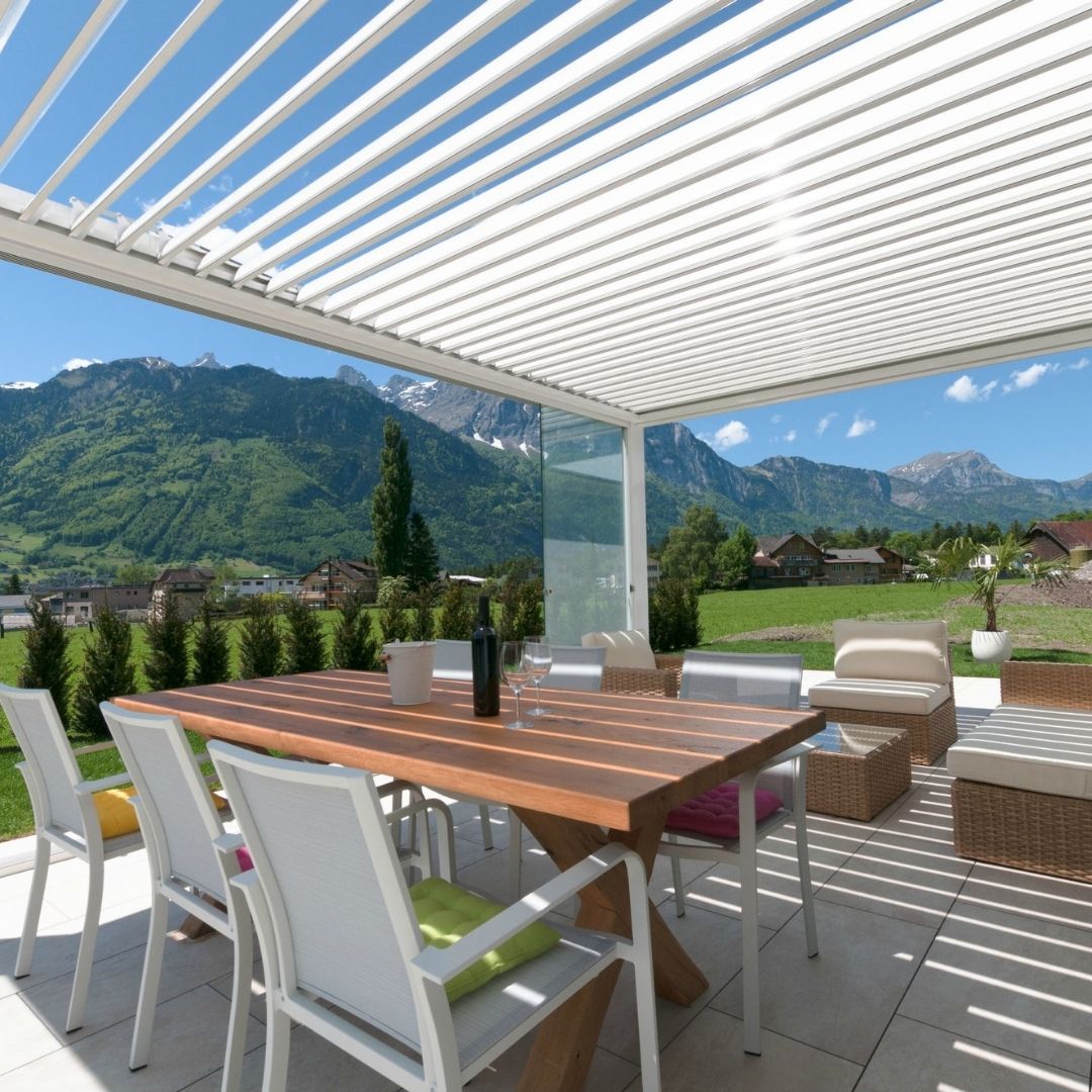 Weisses SKL 100 Lamellendach mit Glaswänden und Blick auf die Schweizer Alpen.