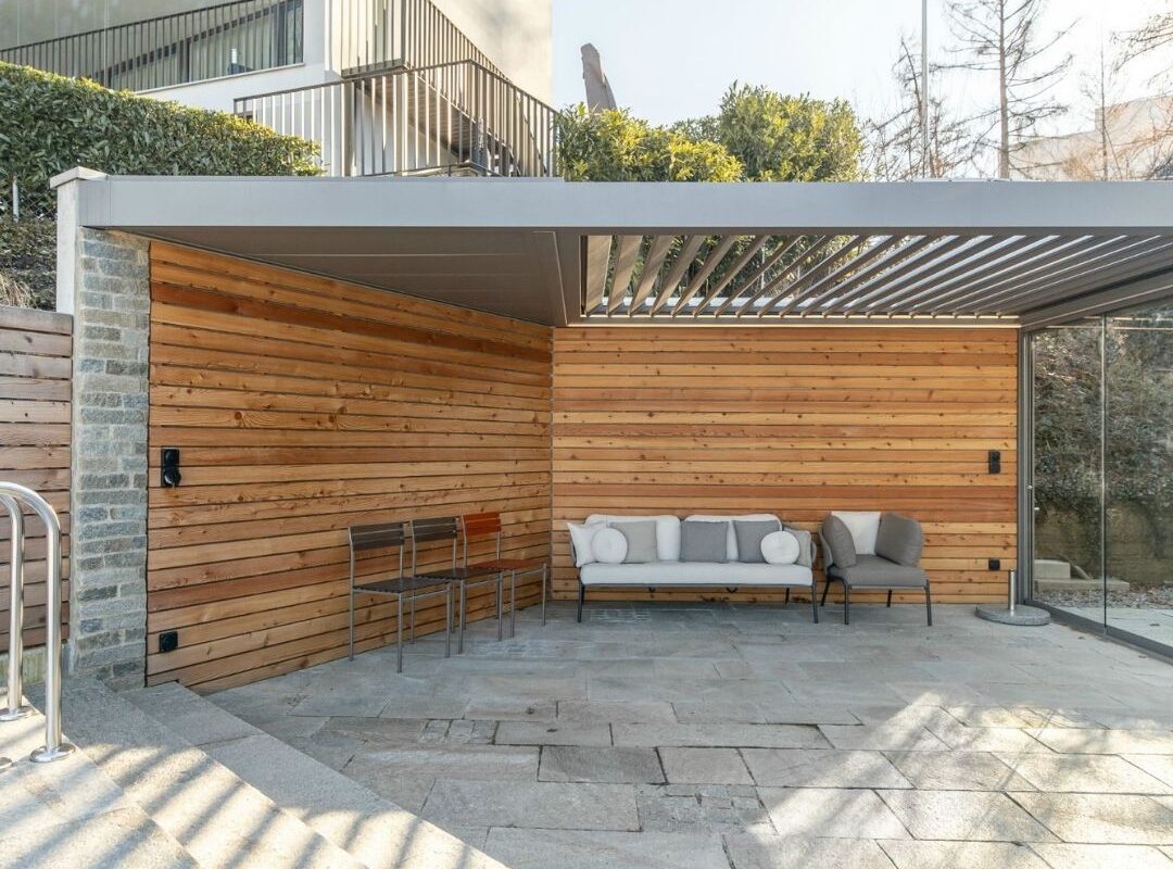 SKL 100 Lamellendach in Horgen, Zürich – überdachte Lounge mit Natursteinboden und Holzverkleidung, wetterfest und stabil bei üblicher Schneelast.