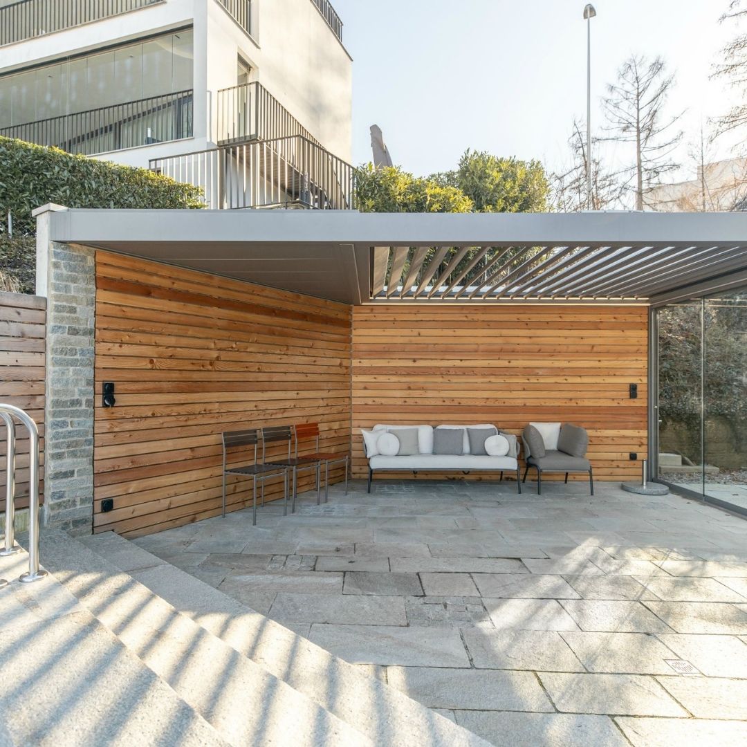 SKL 100 Lamellendach in Horgen, Zürich – überdachte Lounge mit Natursteinboden und Holzverkleidung, wetterfest und stabil bei üblicher Schneelast.