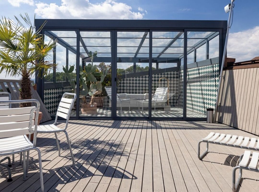 Glasdach Orangerie auf Dachterrasse in Kloten mit Glaswänden und eleganter Konstruktion, schützt Pflanzen im Winter und dient im Sommer als Treffpunkt.