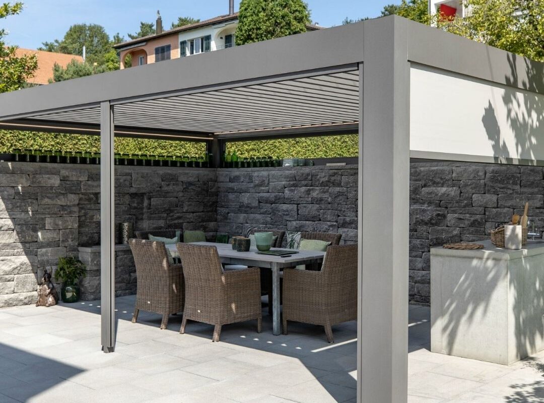 SKL 140 Lamellendach in Küsnacht Zürich mit Natursteinmauer und integriertem Essbereich mit Gartentisch und Korbstühlen.