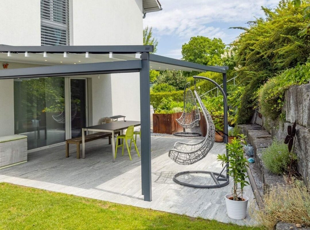 Grosszügige Terrasse mit modernem Textildach in Henggart Zürich, ausgestattet mit Hängesesseln und LED-Beleuchtung.