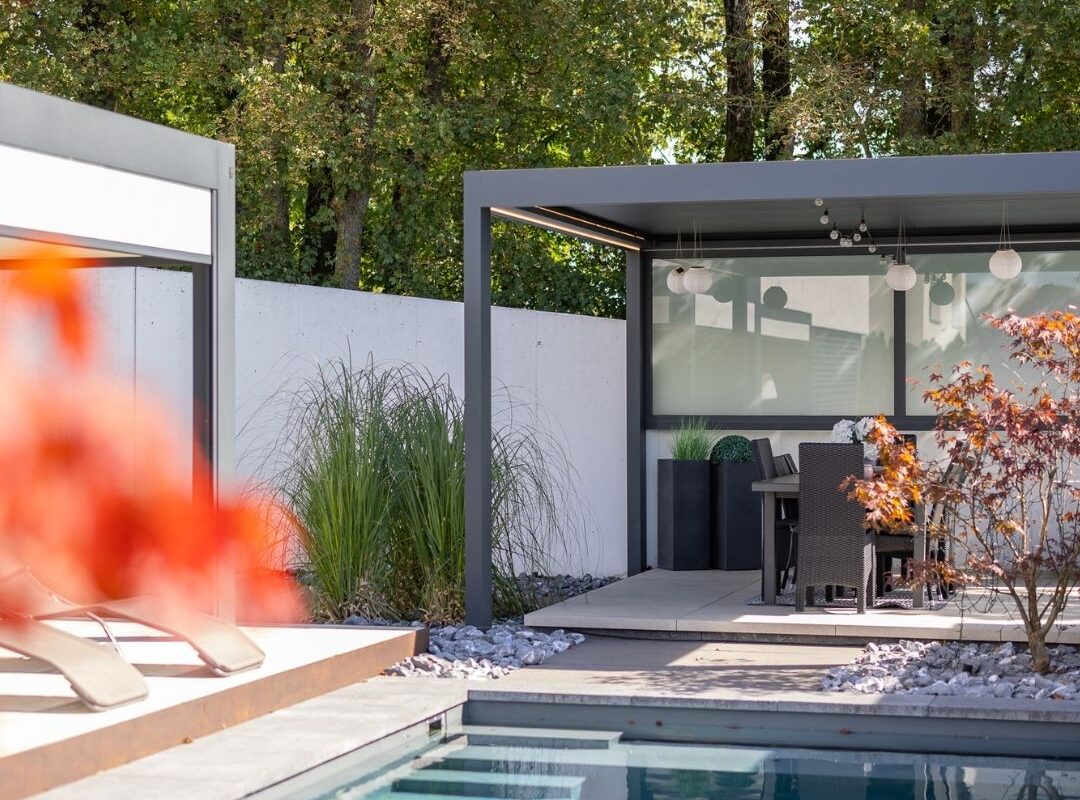 SKL 100 Lamellendach mit seitlicher Verglasung am Pool – moderner Essbereich mit Pflanzen und stimmungsvoller Dekoration.