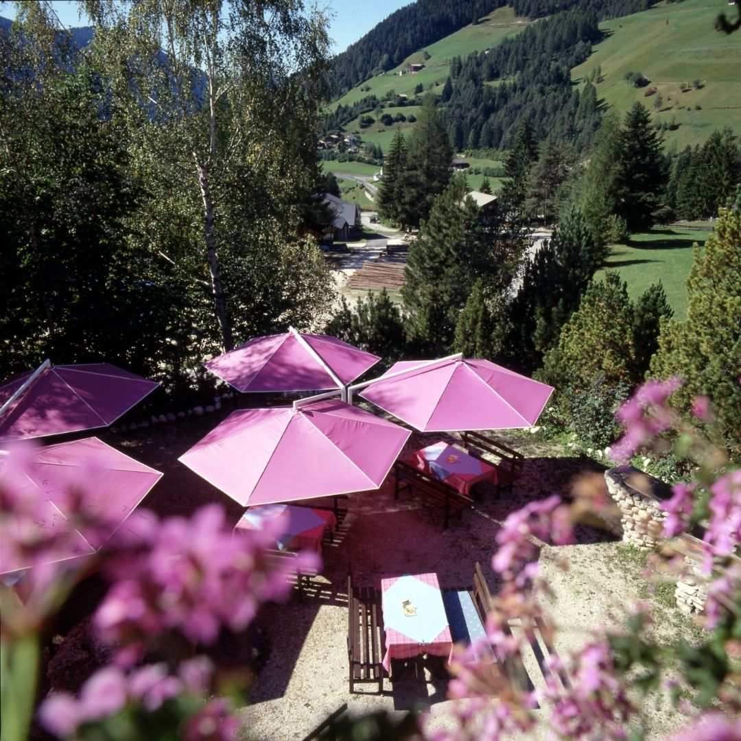 Pinkfarbene RIALTO Sonnenschirme auf einer Restaurantterrasse mit Blick auf die Berge.