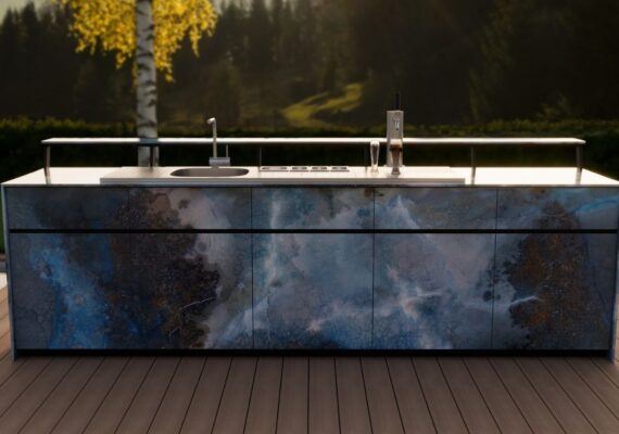 Theiss Outdoor-Bar mit blauen Steinfronten, Spülbecken und Zapfanlage auf Terrasse im Abendlicht mit Wald- und Bergkulisse.
