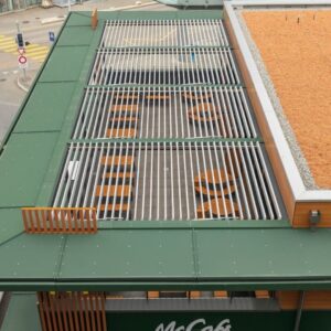Vogelperspektive auf ein McCafé mit grosszügigem Lamellendach, das den Aussenbereich optimal beschattet und in die Gebäudearchitektur integriert ist.