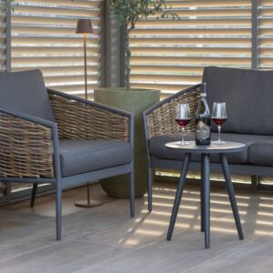 Zwei Outdoor Lounge-Sessel mit grauen Kissen, Rattandetails und kleinem runden Tisch mit Rotwein, im überdachten Aussenbereich von Nook.