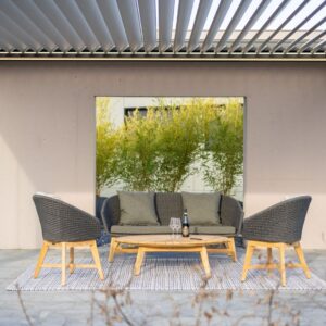 Outdoor-Sitzgruppe von Nook mit Sofa, Sesseln und Couchtisch aus Holz und Geflecht, platziert auf einem Teppich unter einer Überdachung.