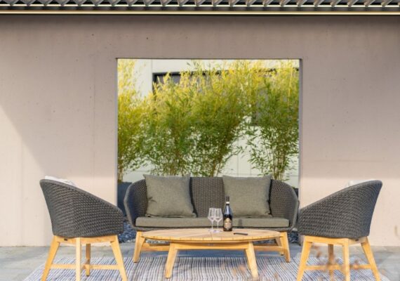 Outdoor-Sitzgruppe von Nook mit Sofa, Sesseln und Couchtisch aus Holz und Geflecht, platziert auf einem Teppich unter einer Überdachung.