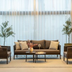 Elegante Nook Outdoor-Lounge mit Sofa, Sesseln, Beistelltischen und dekorativen Kissen vor einem hellen Vorhang.