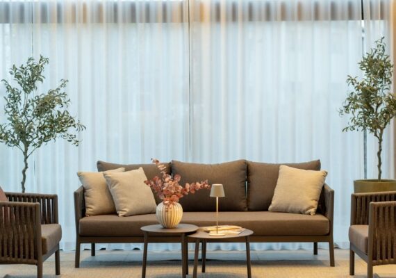 Elegante Nook Outdoor-Lounge mit Sofa, Sesseln, Beistelltischen und dekorativen Kissen vor einem hellen Vorhang.