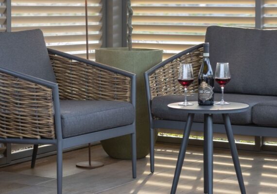 Zwei Outdoor Lounge-Sessel mit grauen Kissen, Rattandetails und kleinem runden Tisch mit Rotwein, im überdachten Aussenbereich von Nook.