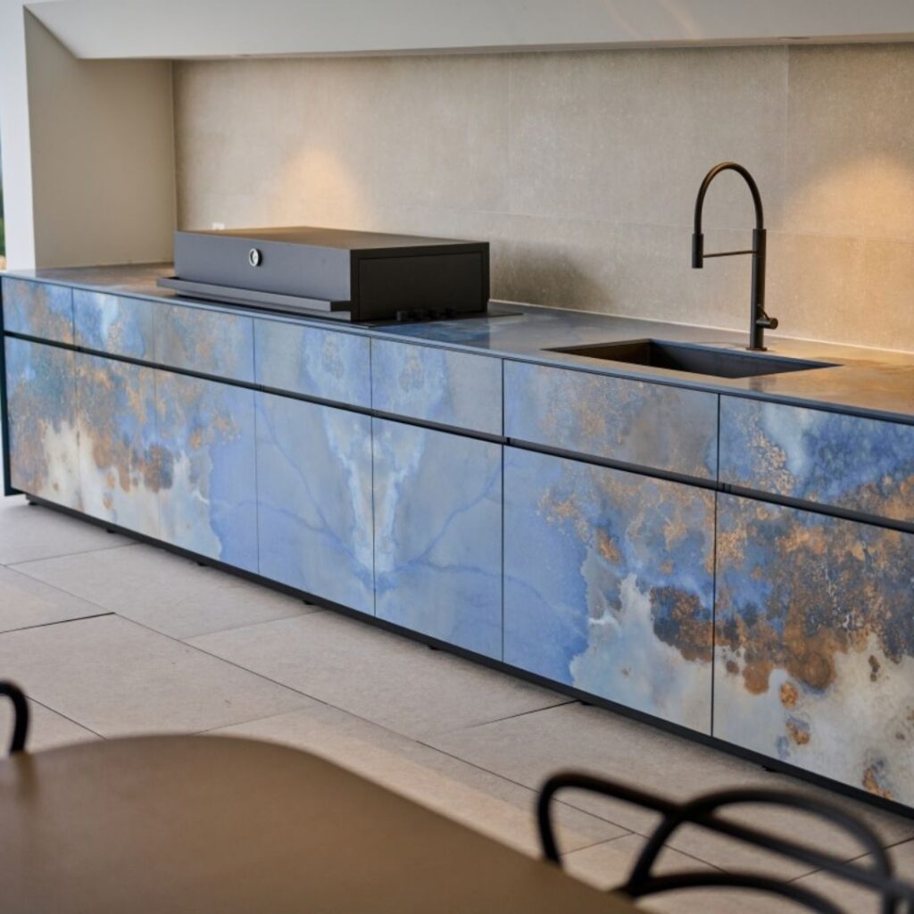 Exklusive Outdoor Küche mit modernem Design in Blau- und Naturtönen, ausgestattet mit Grill und Spülbecken.