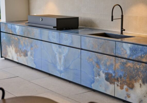 Exklusive Outdoor Küche mit modernem Design in Blau- und Naturtönen, ausgestattet mit Grill und Spülbecken.