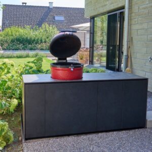 Outdoor Küche mit schwarzer Verkleidung und integriertem roten Keramikgrill im Garten.