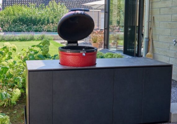 Outdoor Küche mit schwarzer Verkleidung und integriertem roten Keramikgrill im Garten.