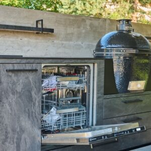 Outdoor Küche im dunklen Stein-Look mit integriertem Keramikgrill und geöffneter Geschirrspülmaschine.