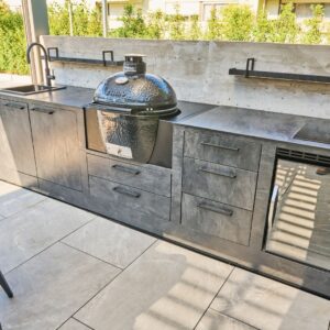 Outdoor Küche im dunklen Stein-Look mit integriertem Keramikgrill, Spülbecken und Kühlschrank.