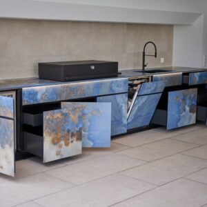 Outdoor Küche mit blauen Natursteinfronten und geöffneten Schubladen sowie Einbaugeräten.