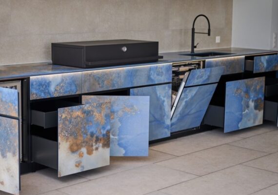 Outdoor Küche mit blauen Natursteinfronten und geöffneten Schubladen sowie Einbaugeräten.