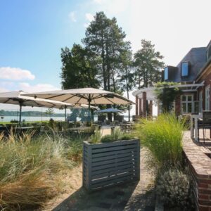Mehrere grossflächige Sonnenschirme spenden Schatten auf einer Restaurantterrasse mit Blick auf den See.
