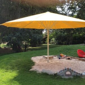 Gelber Sonnenschirm spendet Schatten über einem Sandkasten auf einer Grünfläche.