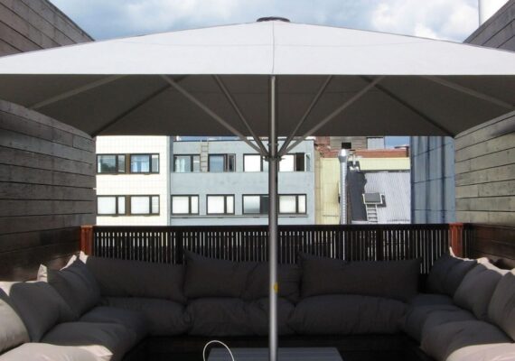 Moderner Sonnenschirm auf einer Dachterrasse mit gemütlicher Lounge und Stadtblick.