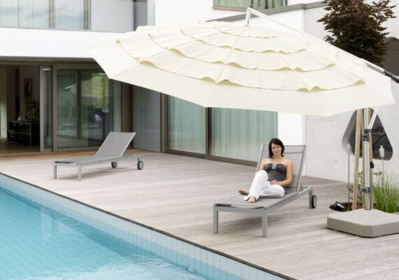 Beiger Sonnenschirm auf einer Poolterrasse mit Liegestühlen und moderner Architektur im Hintergrund.