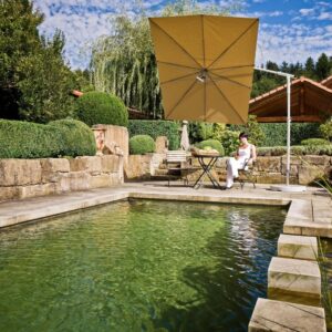 Moderner Sonnenschirm in Gelb spendet Schatten über einem Naturpool mit Sitzgelegenheit und stilvoller Gartengestaltung.