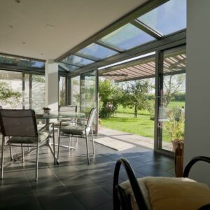 Moderner Wintergarten mit Glasdach und Schiebetüren, ausgestattet mit einem Esstisch und Blick in den Garten.