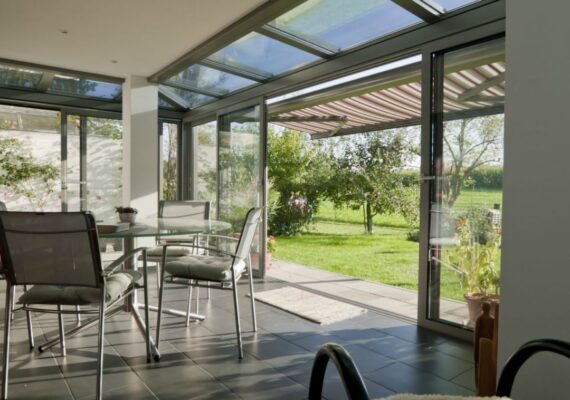Moderner Wintergarten mit Glasdach und Schiebetüren, ausgestattet mit einem Esstisch und Blick in den Garten.