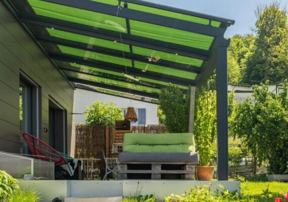 Glasdach mit grüner Beschattungsmarkise über einer Terrasse mit Lounge im Garten.
