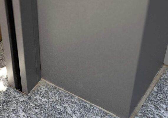 Detailaufnahme einer stabilen Aluminiumstütze eines Lamellendachs auf Steinboden.