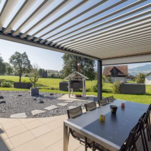 Lamellendach mit grossem Esstisch und Blick in den Garten, moderne Überdachung für gesellige Stunden im Freien.