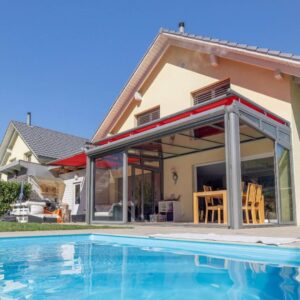 Glasdach mit roter Beschattungsmarkise an einer Terrasse direkt am Pool, kombiniert mit Glaswänden und Essbereich.