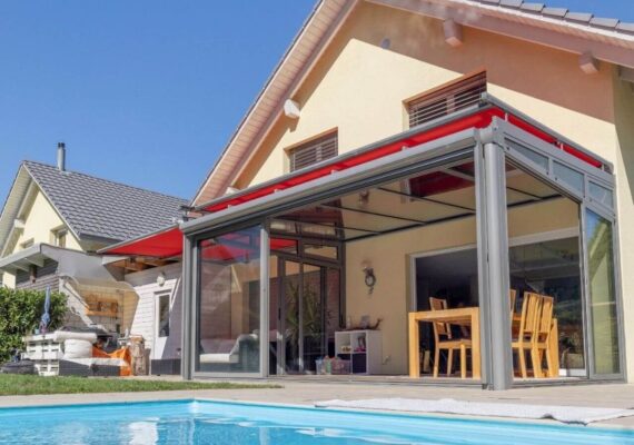 Glasdach mit roter Beschattungsmarkise an einer Terrasse direkt am Pool, kombiniert mit Glaswänden und Essbereich.