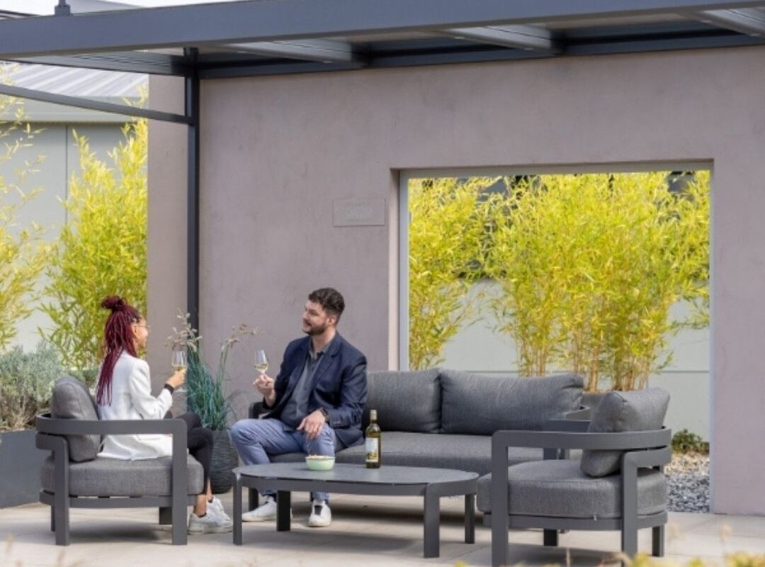 Glasdach mit moderner Lounge im Garten, zwei Personen sitzen entspannt bei einem Glas Wein.