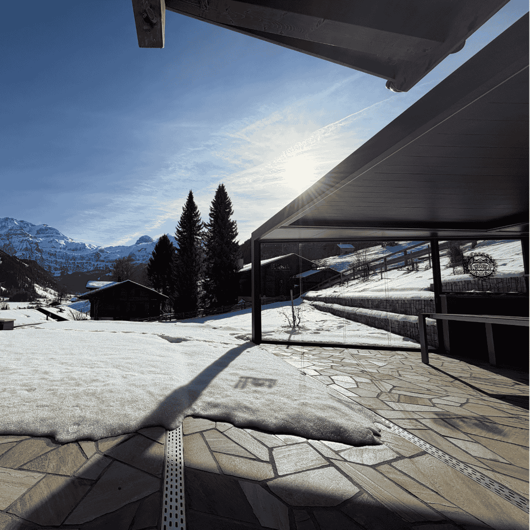 Lamellendach in Sonderform mit Ganz-Glas-Schiebeanlage auf einer Terrasse in Lenk im Simmental bei winterlichen Bedingungen mit Schnee und Bergpanorama.