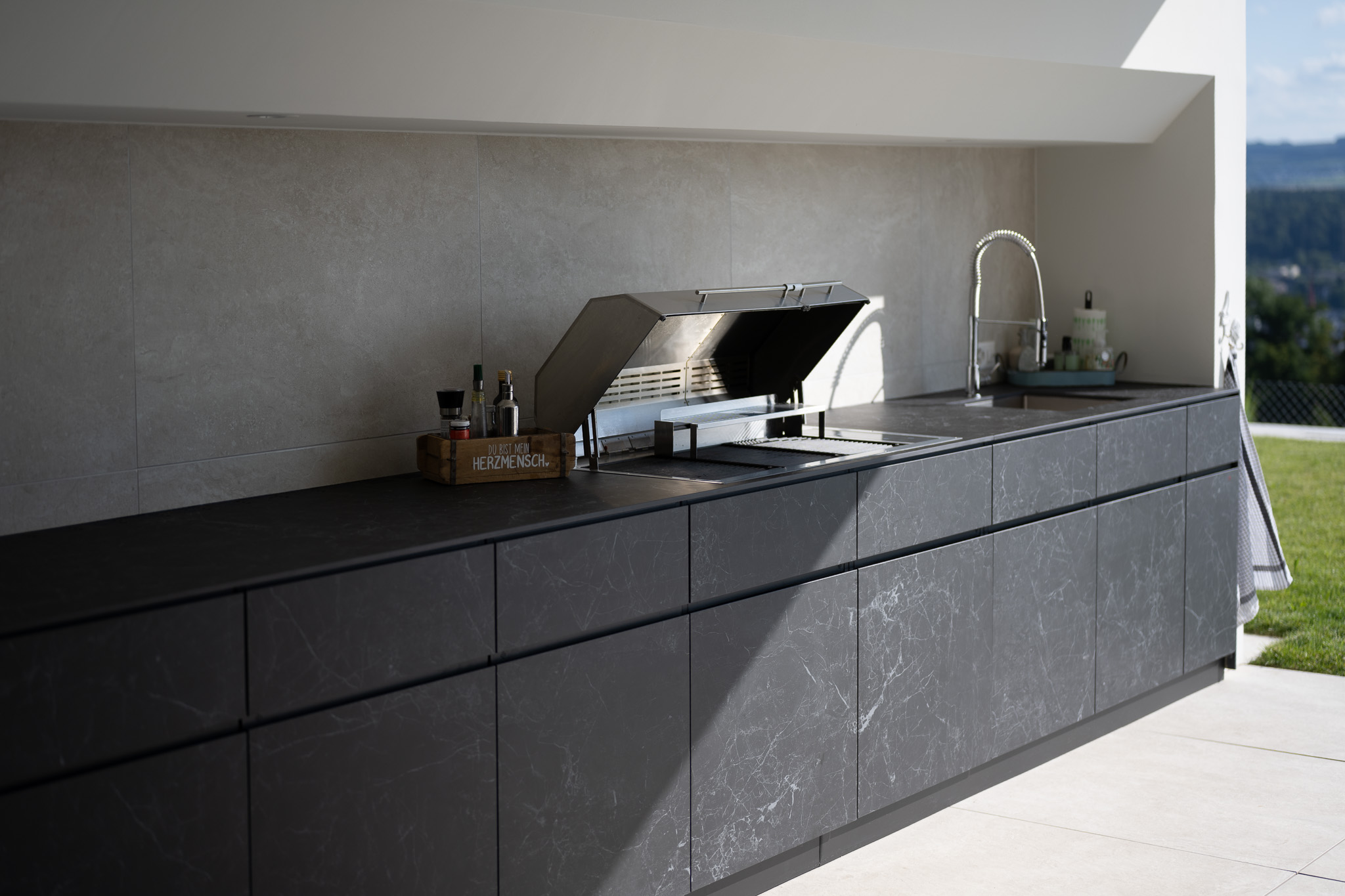 Moderne Aussenküche Theiss Avers in Keramik Nero Greco mit integriertem Elektro Grill und Spülbecken auf einer privaten Terrasse in Widen