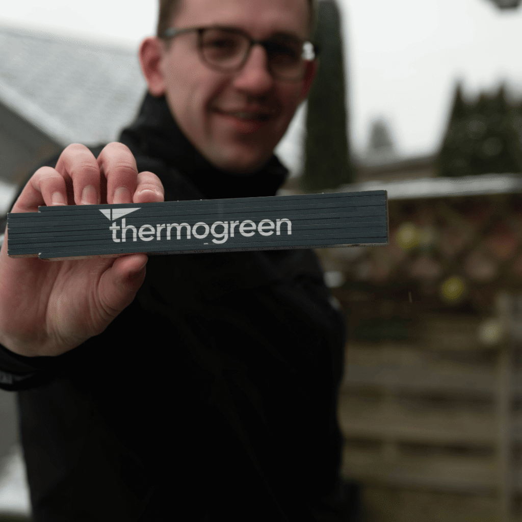 Projektberater von Thermogreen hält einen Thermogreen Meter als Werbegeschenk in die Kamera während eines Beratungstermins im Aussenbereich.