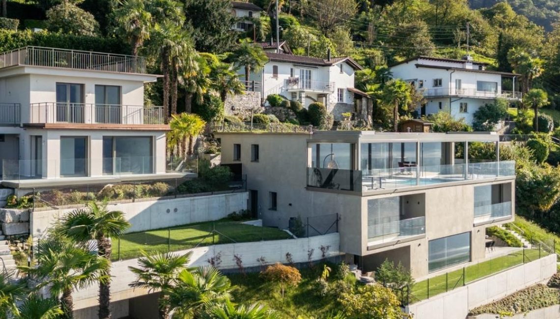 Gesamtansicht eines privaten Wohnhauses in Hanglage in Gerra im Tessin mit integriertem Lamellendach auf der Terrasse und Blick in die begrünte Umgebung.