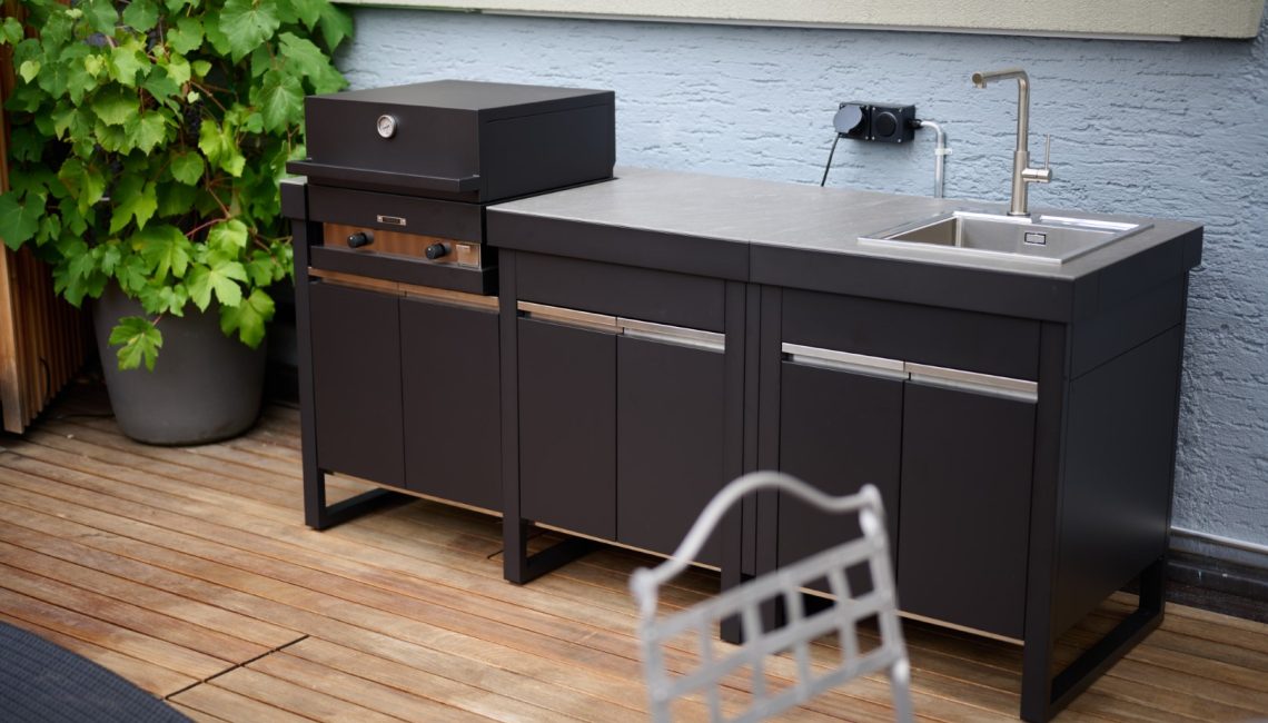 Aussenküche mit geschlossenem Grillmodul und integriertem Spülbecken auf Holzterrasse