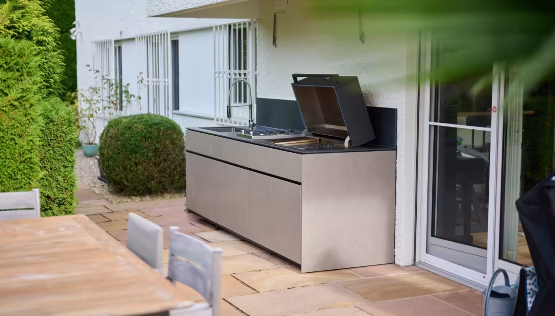 Aussenküche mit geöffnetem Grill integriert in private Gartenterrasse