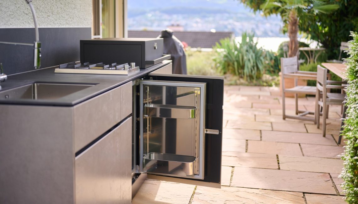 Aussenküche mit geöffnetem Kühlschrank und Blick in den Garten