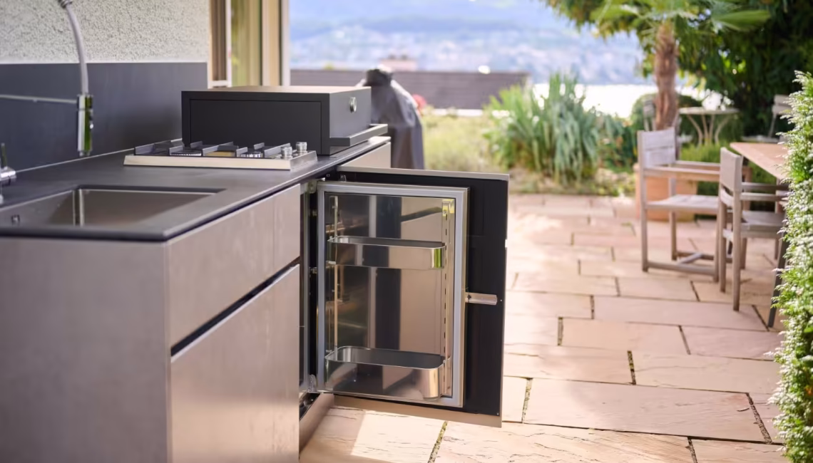 Aussenküche mit geöffnetem Kühlschrank und Blick in den Garten