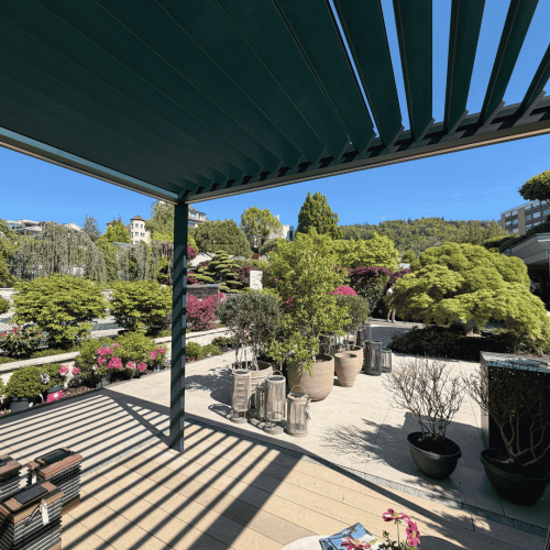 Modernes Lamellendach von Thermogreen bei Hoffmann Gartenbau mit geöffneten Lamellen, stilvoller Terrassenfläche und Blick auf eine hochwertige Gartenlandschaft mit Bäumen, Pflanzen und klarer Architektur.