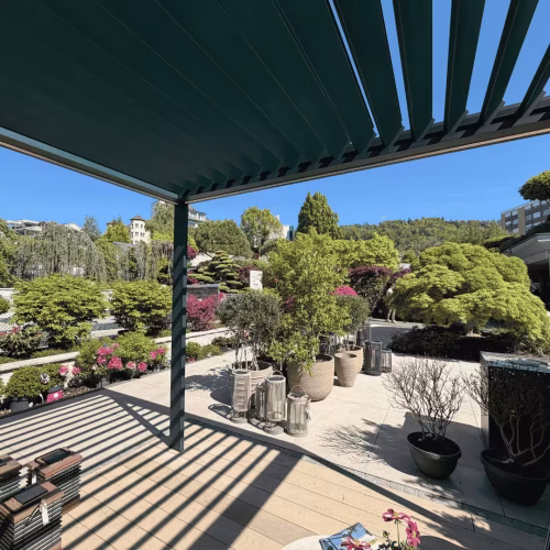 Modernes Lamellendach von Thermogreen bei Hoffmann Gartenbau mit geöffneten Lamellen, stilvoller Terrassenfläche und Blick auf eine hochwertige Gartenlandschaft mit Bäumen, Pflanzen und klarer Architektur.