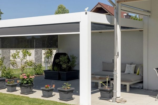 SKL 140 Lamellendach in Weiss an einem Einfamilienhaus mit seitlichem Sonnenschutz und gemütlicher Lounge.