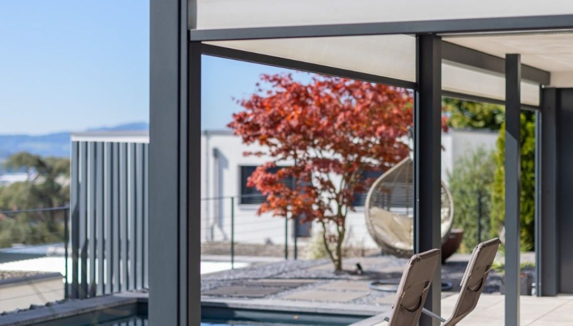 SKL 140 Lamellendach mit zwei Liegestühlen am Pool – moderner Outdoor-Bereich mit japanischem Ahorn und Hängesessel im Hintergrund.